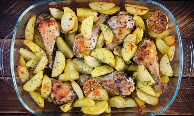 Delizioso pollo al forno con patate, erbe aromatiche e spicchi d'aglio arrostiti, servito in una teglia di vetro.