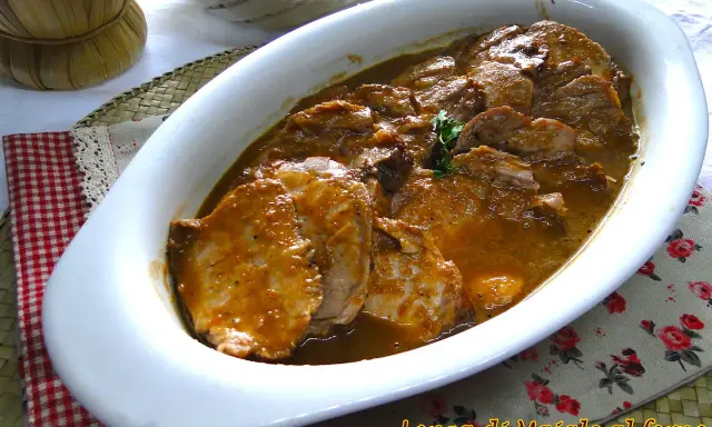 Arrosto di maiale morbido con sughetto, servito in una teglia bianca, pronto per essere gustato.