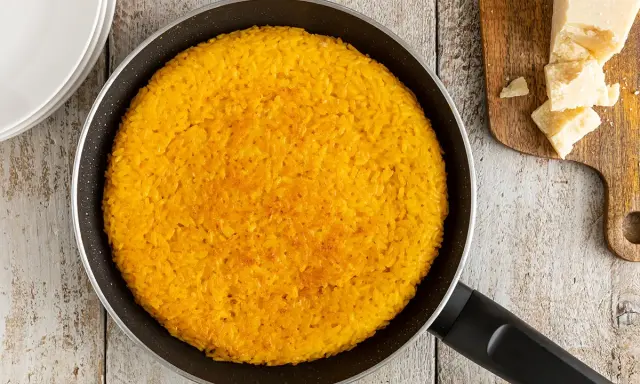 Un invitante riso al salto dorato in padella, pronto per essere gustato con scaglie di Parmigiano Reggiano.