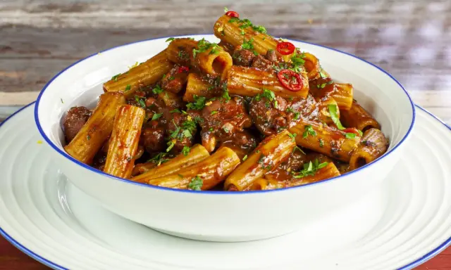Rigatoni conditi con un ricco ragù di polpo, guarniti con prezzemolo fresco e peperoncino.