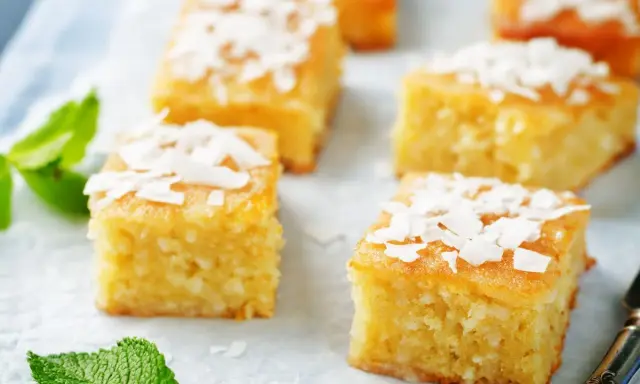 Deliziosi quadretti di torta al cocco, guarniti con scaglie di cocco e foglioline di menta fresca.