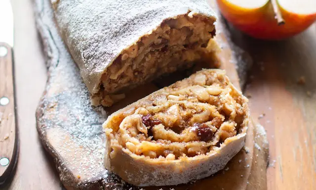 Delizioso strudel di mele con pasta sfoglia, cosparso di zucchero a velo, su un tagliere di legno.