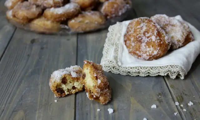 Frittelle di riso ricetta della nonna: dolcetti dorati e zuccherati, alcuni su un piatto, altri su un pizzo, uno aperto rivela l'interno morbido.