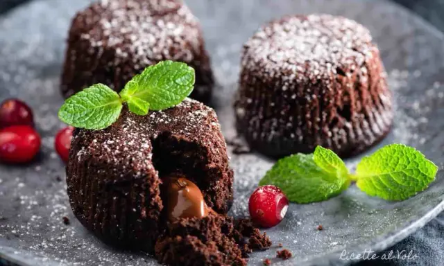 Tre tortini al cioccolato con cuore fondente, guarniti con menta e frutti rossi, spolverati di zucchero a velo.