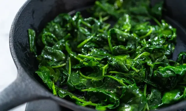 Spinaci freschi e lucidi che sfrigolano in una padella di ghisa, pronti per essere gustati.