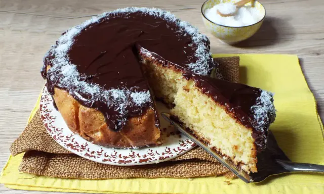 Deliziosa torta cocco e cioccolato, con una fetta appena tagliata e cosparsa di cocco grattugiato.