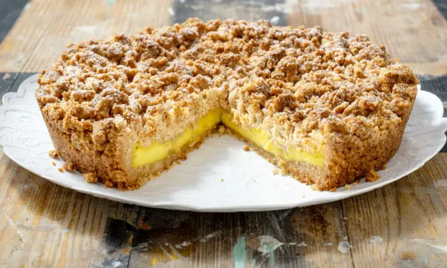 Sbriciolata alla crema con una crosta dorata e un ripieno giallo brillante, cosparsa di zucchero a velo.