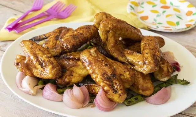 Alette di pollo in padella, dorate e succulente, servite con cipolle rosse e asparagi su un piatto bianco.