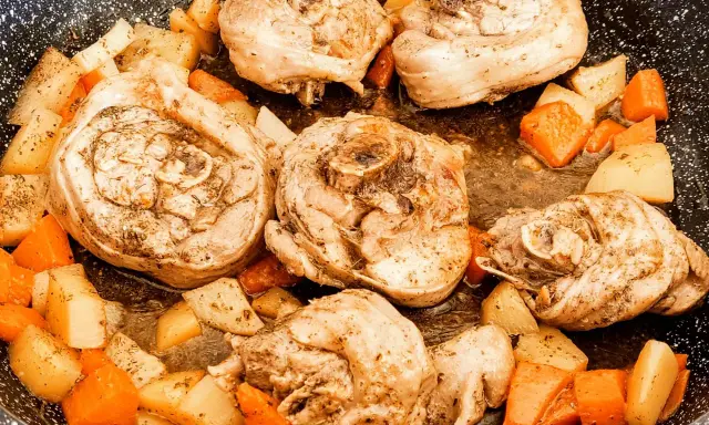 Porzioni di ossobuco di tacchino cotte in padella con patate e carote a cubetti, condite con erbe aromatiche.
