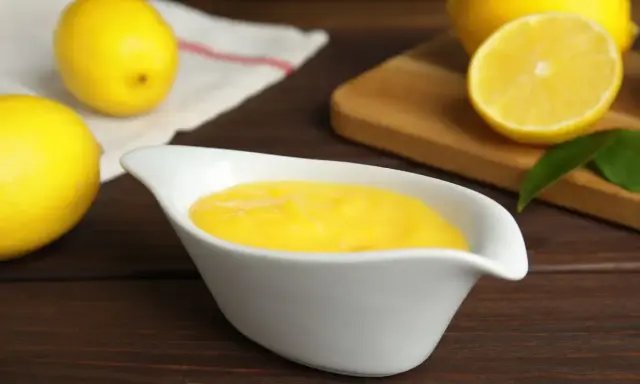 Una ciotola bianca contiene una vellutata crema al limone, con limoni freschi sullo sfondo.