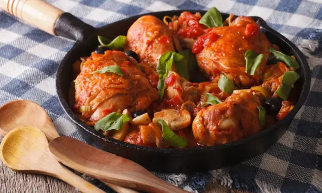Pezzi di coniglio alla cacciatora in padella con pomodoro, olive e basilico, pronti per essere gustati.