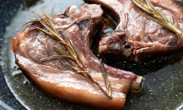Due braciole di maiale succulente cuociono in padella con rametti di rosmarino.