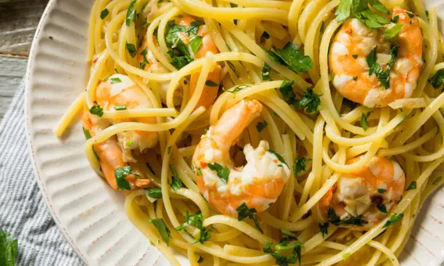 Un piatto invitante di pasta con gamberetti, condita con prezzemolo fresco e servita su un piatto bianco.