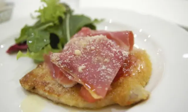 Cotoletta alla bolognese dorata, coperta da prosciutto crudo e parmigiano, con un contorno di insalata fresca.