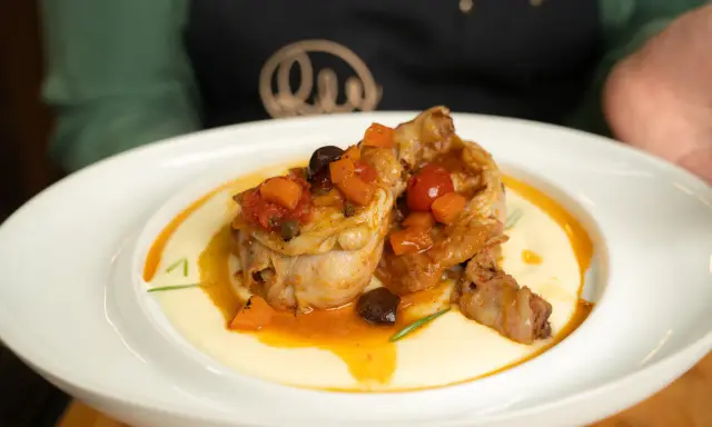 Pollo alla cacciatora ricetta della nonna: succulenti pezzi di pollo in umido con pomodoro, olive e carote, serviti su un letto di polenta cremosa.