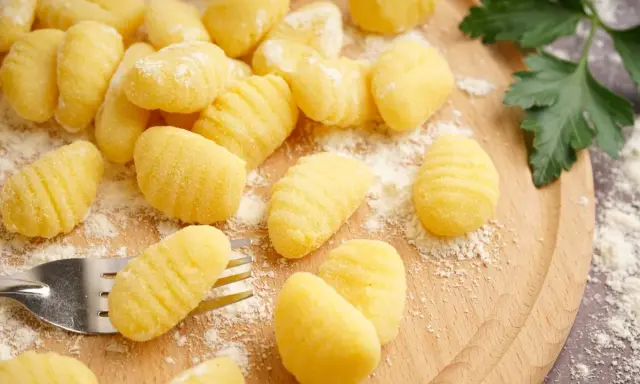 Gnocchi fatti in casa pronti per la friggitrice ad aria, spolverati di farina su un tagliere di legno.