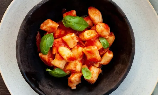Gnocchi di ricotta soffici e saporiti, conditi con un sugo di pomodoro fresco e guarniti con foglie di basilico.