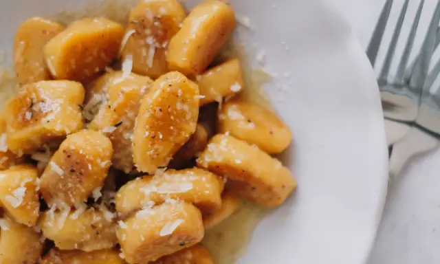 Gnocchi di zucca dorati, conditi con burro fuso, pepe nero e scaglie di parmigiano, pronti per essere gustati.