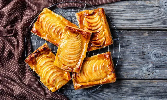 Deliziosi dolci con pasta sfoglia rettangolare, ripieni di mele caramellate, su una griglia di raffreddamento.