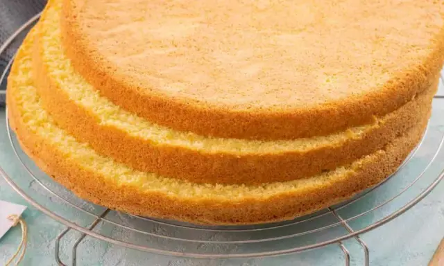Tre soffici strati di pan di spagna senza glutine raffreddano su una griglia. Un'etichetta con scritto "senza glutine" è appesa alla griglia.