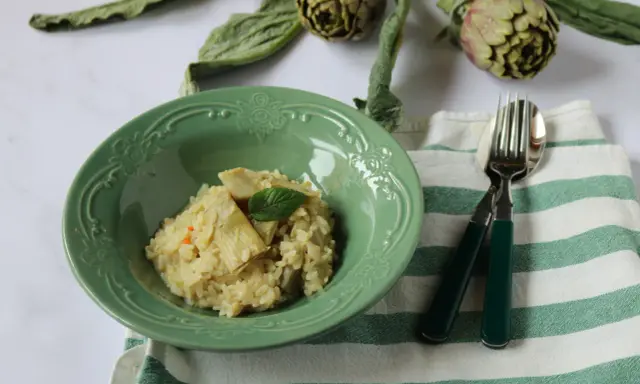 Un cremoso risotto con carciofi freschi, guarnito con una fogliolina di menta, pronto per essere gustato.