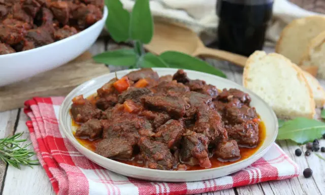 Cinghiale in umido fatto in casa da Benedetta, un piatto ricco e saporito, servito con pane fresco e un bicchiere di vino rosso.