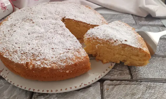 Una soffice torta al latte, spolverata di zucchero a velo, con una fetta appena tagliata pronta per essere gustata.