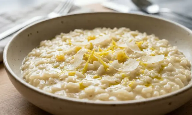 Un cremoso risotto al limone, guarnito con scorza di limone e scaglie di parmigiano, servito in una ciotola rustica.