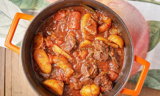 Un saporito spezzatino con patate, cotto lentamente in un tegame arancione, pronto per essere gustato.