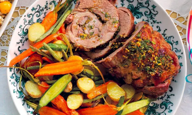Un succulento agnello al forno, affettato e guarnito con erbe aromatiche, servito con patate novelle, carote e fagiolini.