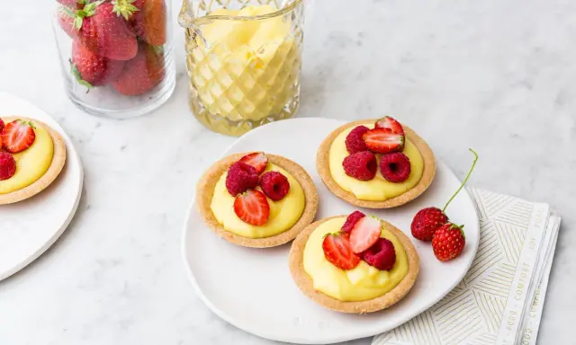 Deliziose tartellette alla frutta con crema pasticcera e frutti di bosco freschi, pronte per essere gustate.