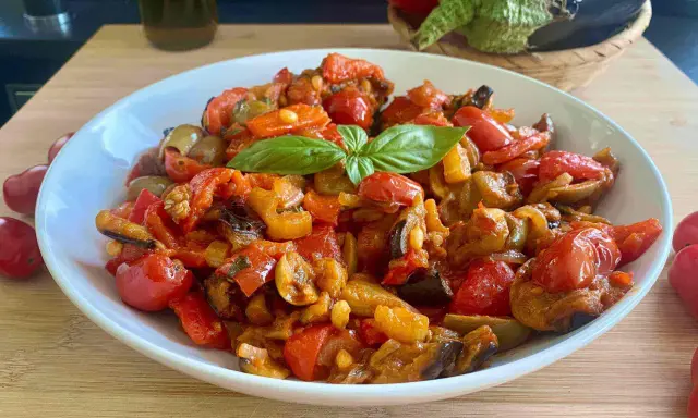 Caponata siciliana ricetta della nonna: melanzane, pomodori, peperoni e basilico in un piatto bianco.