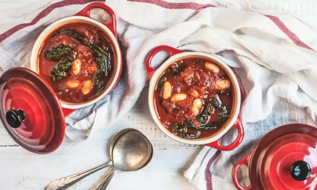 Due ciotole rosse con zuppa di cavolo nero e fagioli, pronte per essere gustate.