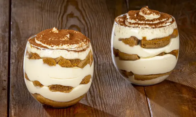 Due bicchieri di delizioso tiramisù senza uova, con strati di savoiardi e crema, spolverati di cacao.