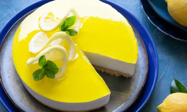 Delizioso cheesecake al limone con glassa gialla brillante, decorato con fette di limone e menta. Una fetta è stata tolta, rivelando la base croccante.