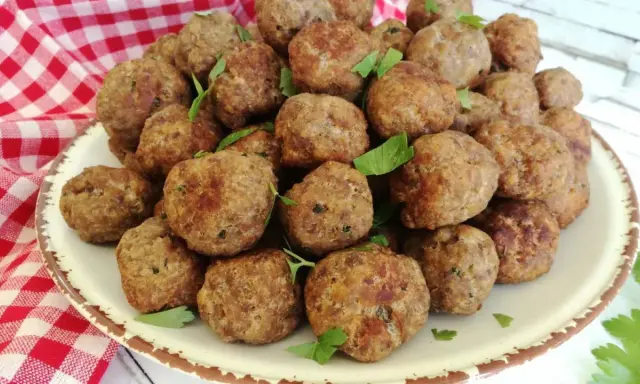 Un piatto colmo di polpette in bianco, dorate e profumate, guarnite con prezzemolo fresco.