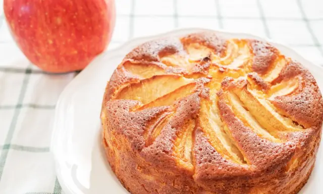 Torta di mele con yogurt, dorata e soffice, con mele a vista. Accanto, una mela rossa fresca.