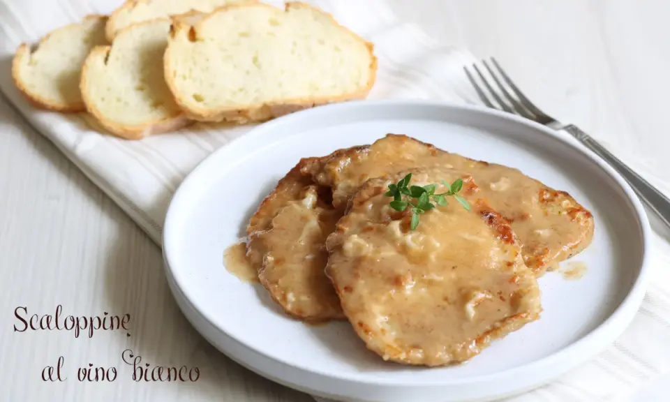 Tre scaloppine al vino bianco su un piatto bianco, guarnite con timo fresco, accompagnate da fette di pane tostato.