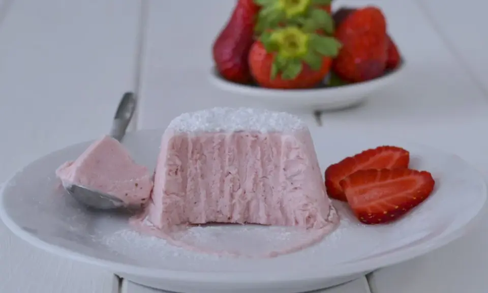 Delizioso semifreddo alle fragole, con una fetta servita su un cucchiaino e guarnito con zucchero a velo e fragole fresche.