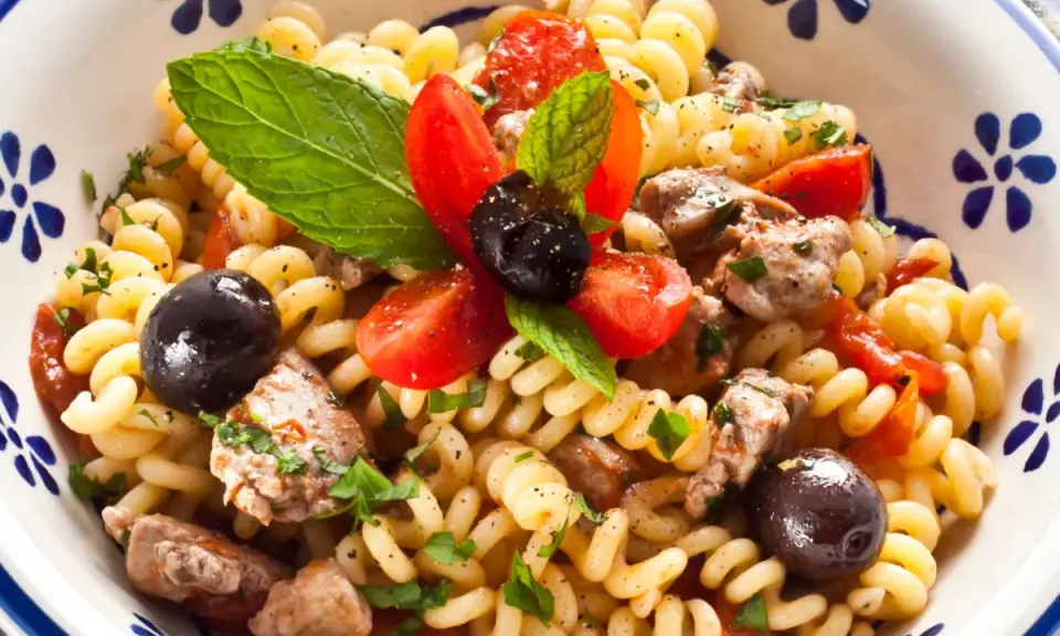 Pasta con pesce spada, pomodorini, olive nere e menta fresca in una ciotola decorata.