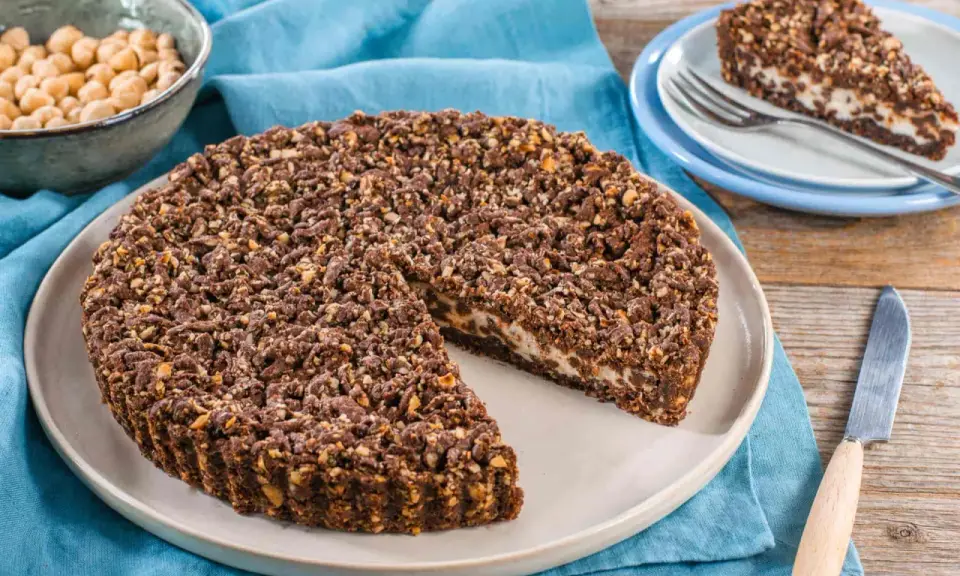 Sbriciolata ricotta e cioccolato con croccante copertura di nocciole. Una fetta è già servita su un piattino.