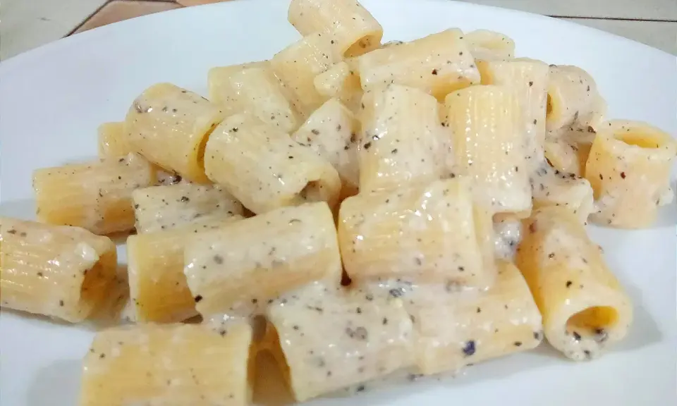 Piatto di rigatoni cremosi conditi con un classico cacio e pepe, pronti per essere gustati.