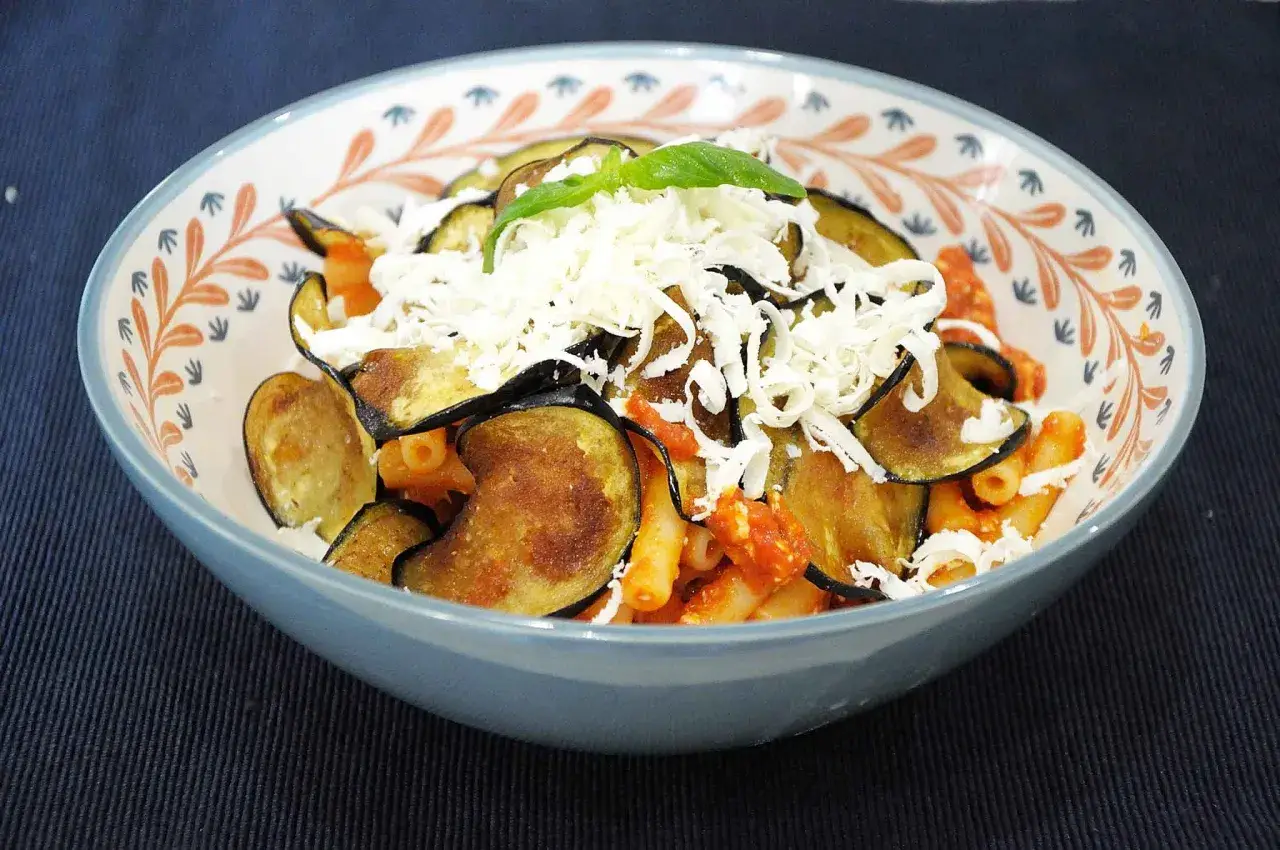 Un piatto di pasta alla norma fumante, con melanzane fritte, sugo rosso e abbondante ricotta salata grattugiata.