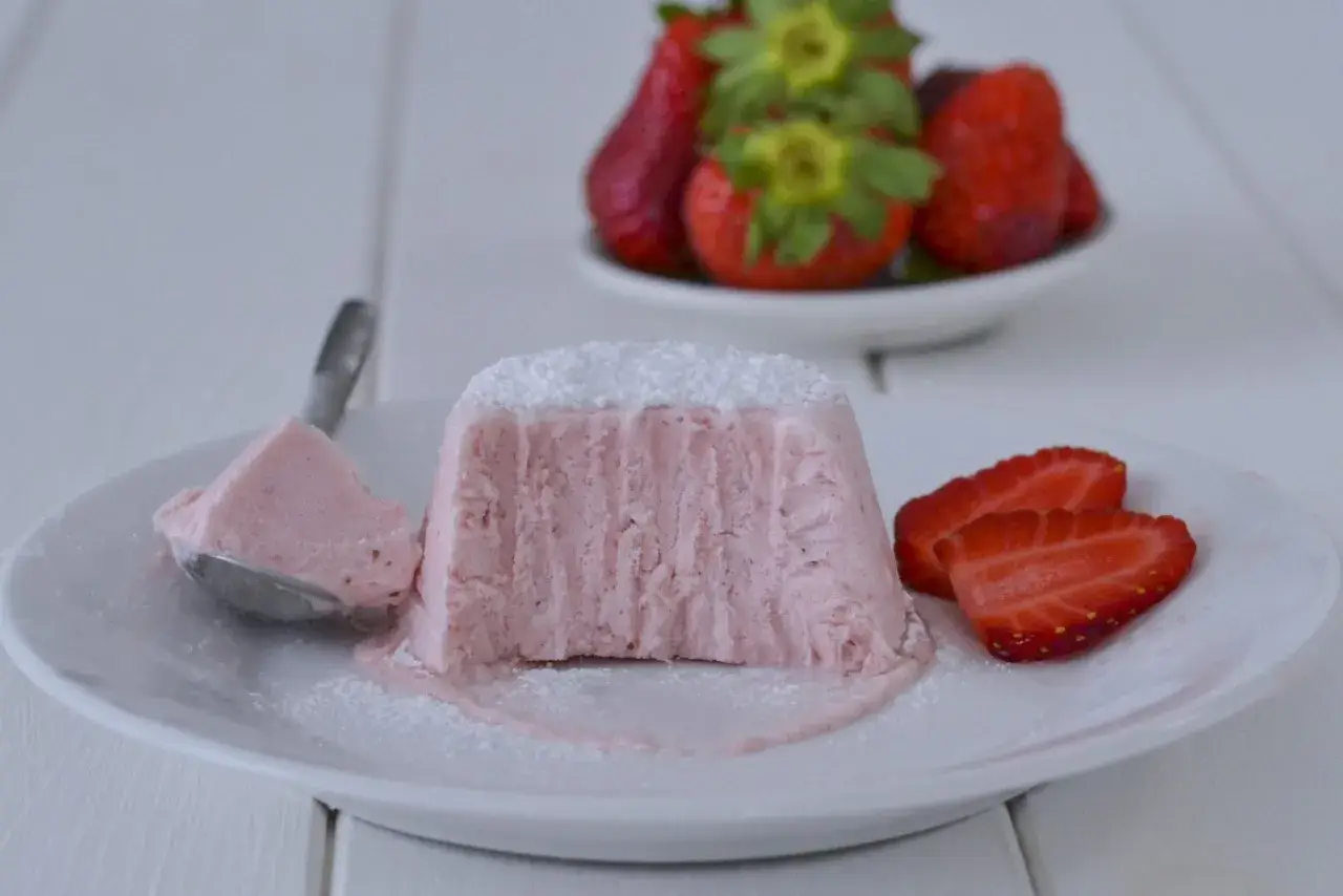 Delizioso semifreddo alle fragole, con una fetta servita su un cucchiaino e guarnito con zucchero a velo e fragole fresche.