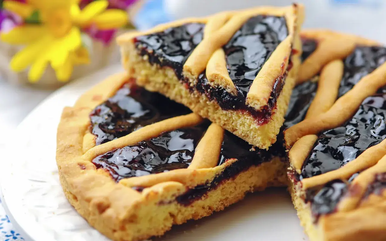 Una fetta di crostata di marmellata, con la sua pasta frolla dorata e il ripieno scuro e lucido, pronta per essere gustata.