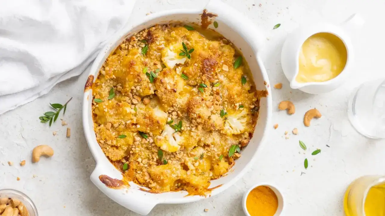 Cavolfiore al forno con pangrattato croccante e formaggio filante, guarnito con erbe fresche e anacardi.