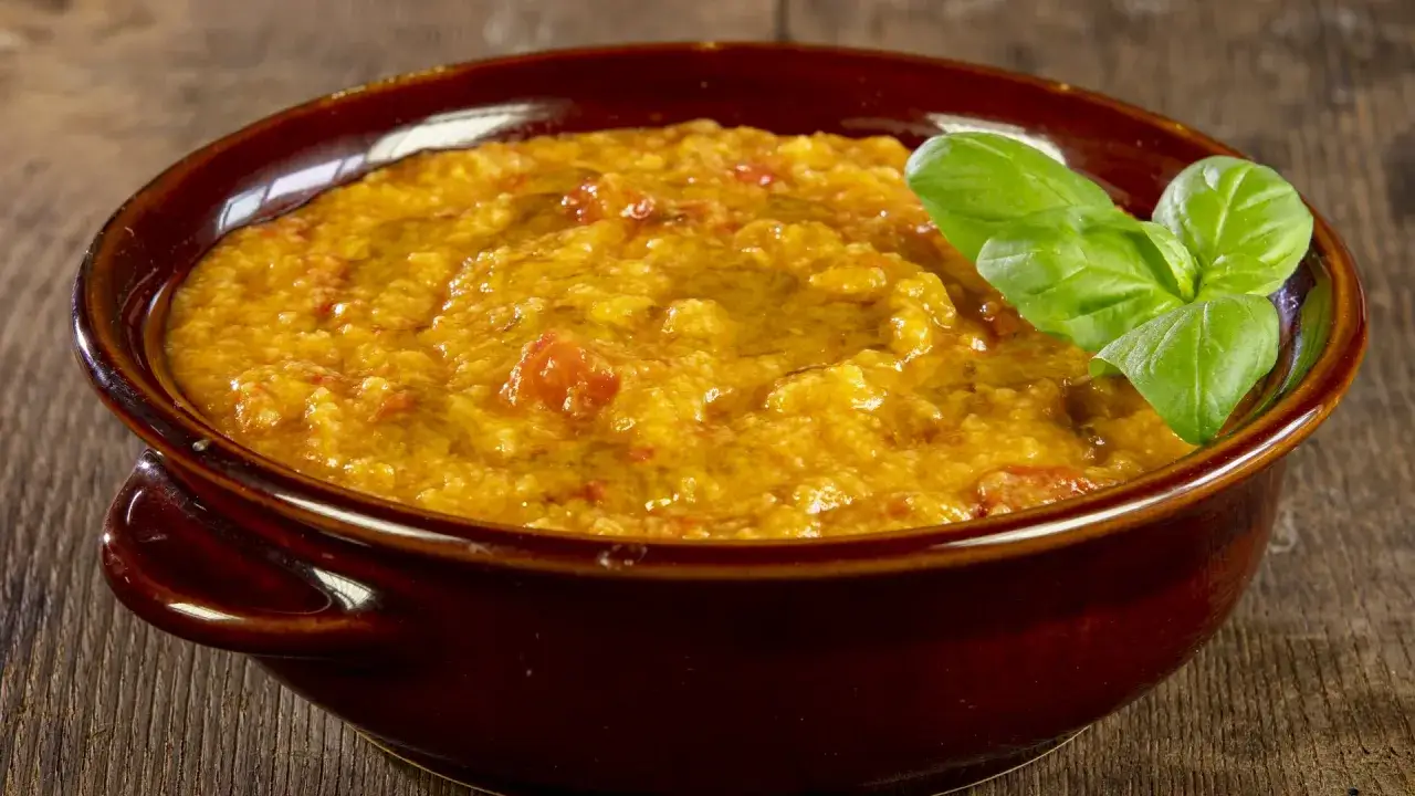 Piatto di pappa al pomodoro fumante, guarnito con basilico fresco e un filo d'olio, servito in una ciotola di terracotta su un tavolo di legno.