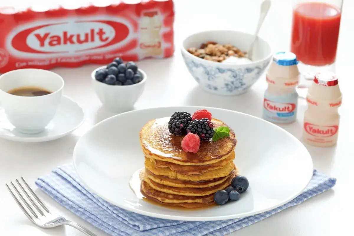 Pancakes con farina di avena, guarniti con frutti di bosco, serviti con caffè, mirtilli, yogurt e Yakult.