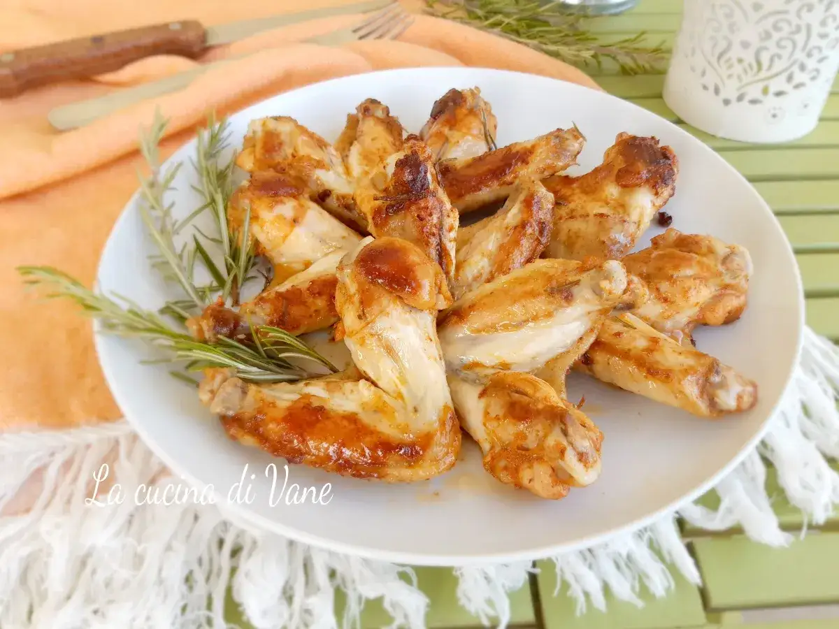 Alette di pollo in padella dorate e succulente, guarnite con rametti di rosmarino fresco.