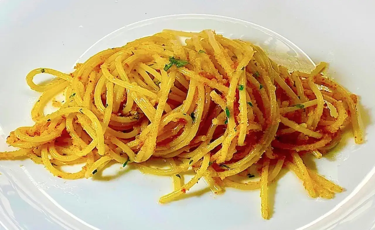 Un piatto di spaghetti conditi con un sugo saporito a base di acciughe e prezzemolo, serviti su un piatto bianco.